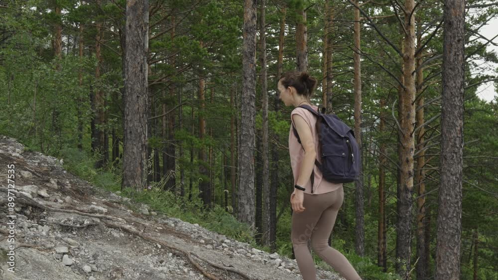 A female tourist with a backpack is trekking in the forest in summer. The concept of hiking and active life in nature. Slow motion A female tourist with a backpack is trekking in the forest in summer. The concept of hiking and active life in nature. Slow motion