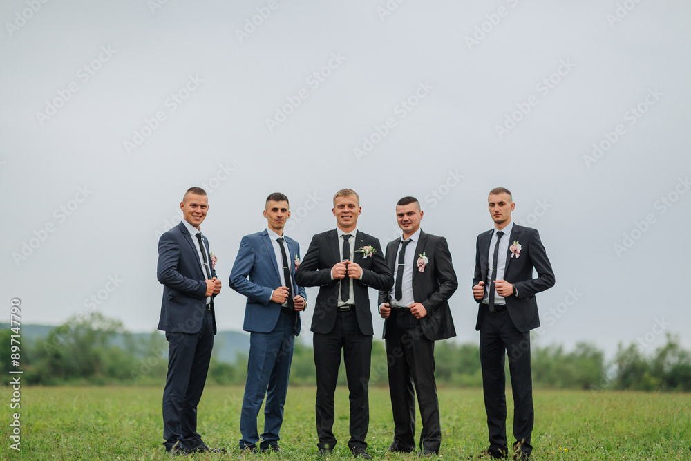 A group of five men are standing in a field, all wearing suits and ties. They are posing for a photo, with one man holding a wine glass. Scene is formal and elegant A group of five men are standing in a field, all wearing suits and ties. They are posing for a photo, with one man holding a wine glass. Scene is formal and elegant