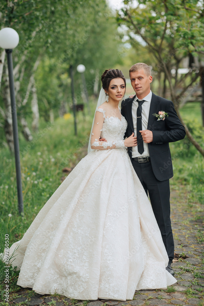 A bride and groom are posing for a picture in a park. The bride is wearing a long white dress and the groom is wearing a suit. Scene is happy and romantic A bride and groom are posing for a picture in a park. The bride is wearing a long white dress and the groom is wearing a suit. Scene is happy and romantic