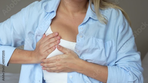 The young blonde woman feeling discomfort in her breast suffering from a pain during period. Cropped shot of a girl checking breast groping for seals on a grey background. Self-examination