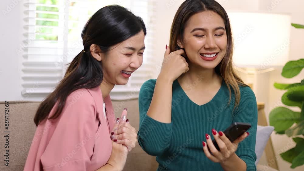 Young Asian woman happily playing with mobile phone and laughing in living room at home. Young Asian woman happily playing with mobile phone and laughing in living room at home.