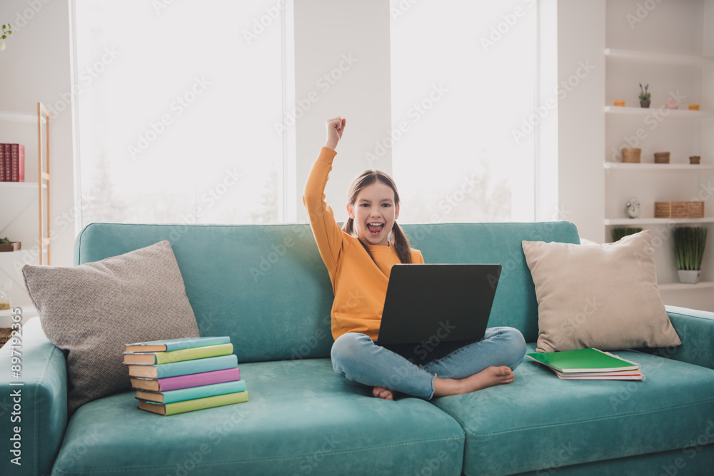 Full body portrait of cute schoolchild sitting couch laptop raise fists study learn flat indoors Full body portrait of cute schoolchild sitting couch laptop raise fists study learn flat indoors