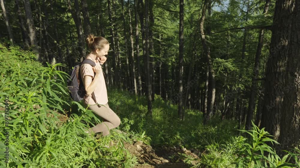 A female tourist with a backpack is trekking in the forest in summer. The concept of hiking and active life in nature. Slow motion A female tourist with a backpack is trekking in the forest in summer. The concept of hiking and active life in nature. Slow motion