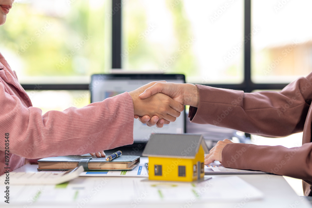 Fototapeta premium Two women shaking hands in front of a yellow house