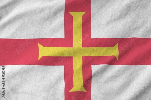 Guernsey flag depicted on folded wavy fabric of old cloth close up photo