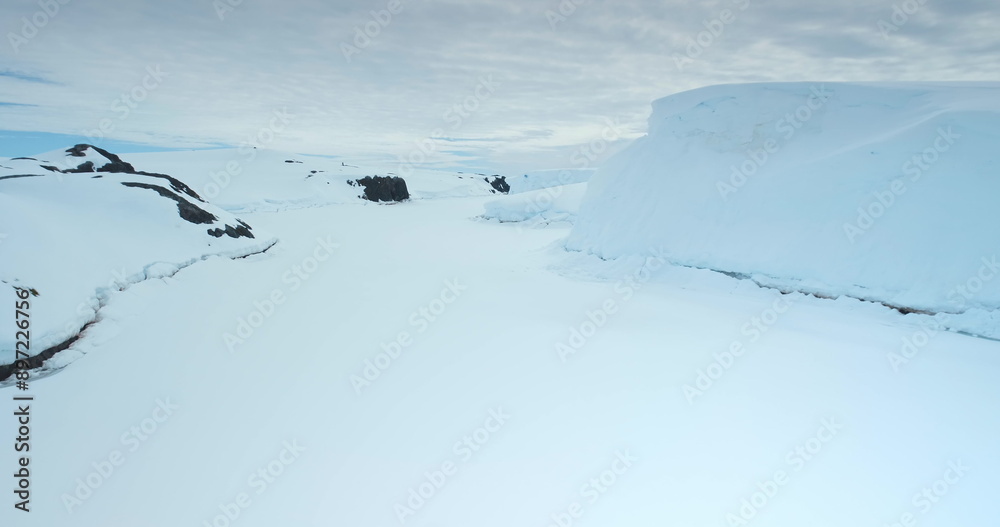 Fly above frozen panorama of Antarctic wild nature. Breathtaking journey over winter snow covered Antarctica landscape. Frozen polar ocean, glacier, rocks. Discover beauty of South Pole. Drone flight