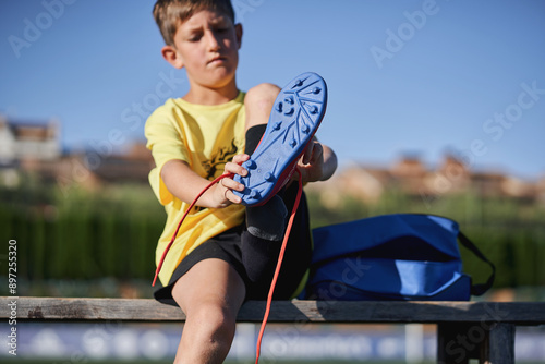 Bilde på lerret Young boy lacing up blue soccer cleats on a bench at the sports field