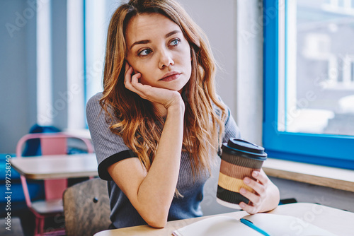 Tired woman feeling bored of exam preparation indoors making coffee break for take energy, unhappy female student exhausted from education and learning indoors holding takeaway caffeine beverage