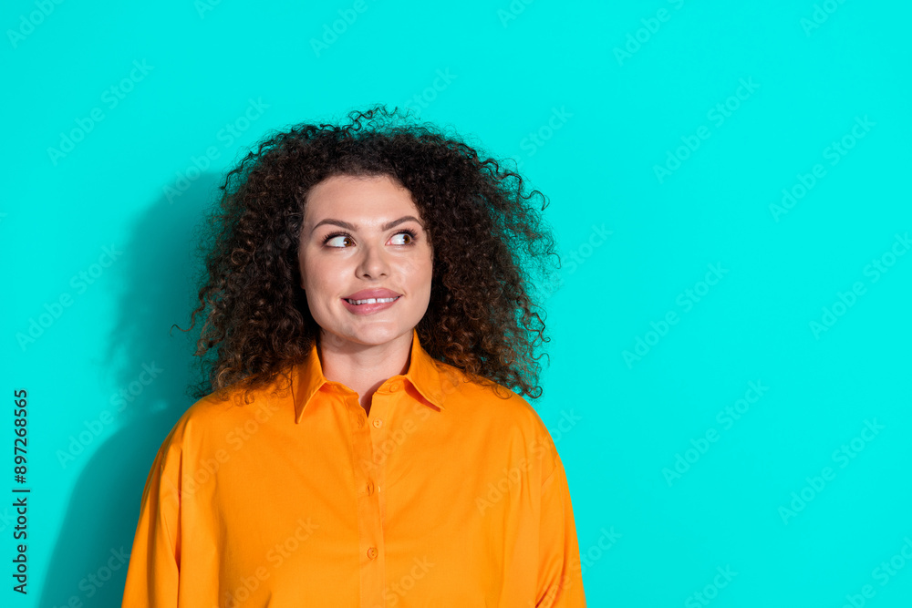 Photo of positive woman with wavy hairstyle dressed orange t-shirt look empty space biting lip isolated on turquoise color background Photo of positive woman with wavy hairstyle dressed orange t-shirt look empty space biting lip isolated on turquoise color background