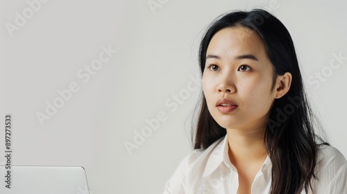 Close-up portrait Asian woman in a minimalist studio, gazing intently, white backdrop and soft natural light thoughtful expression and sleek black hair, creating serene, modern aesthetic.