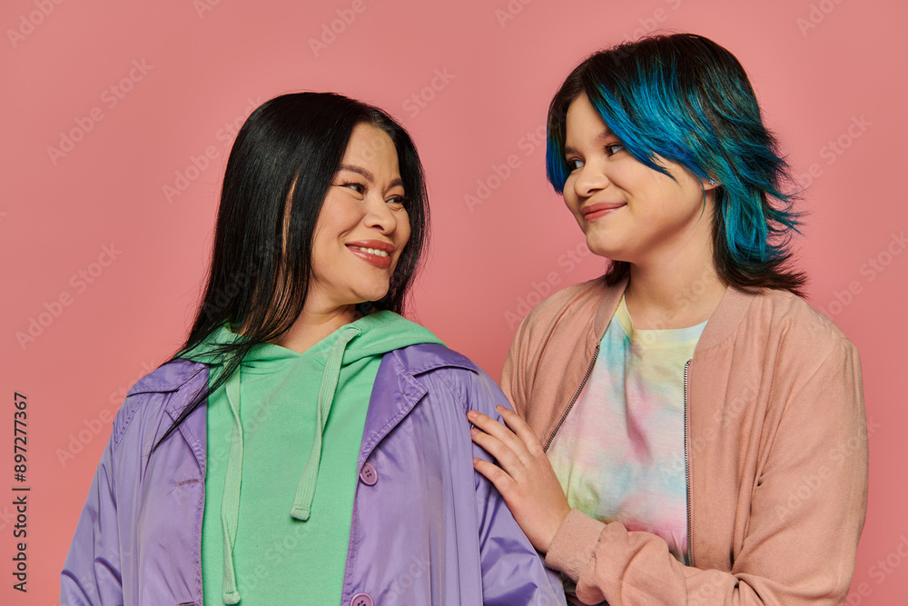 Asian mother and teenage daughter standing together in casual wear in front of a vibrant pink background. Asian mother and teenage daughter standing together in casual wear in front of a vibrant pink background.