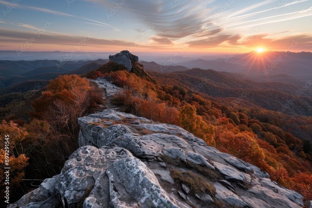 Fototapeta premium The photo showcases a rocky mountain range bathed in the glow of a stunning sunset, with vibrant red and orange autumn trees and a dramatic, open sky above.