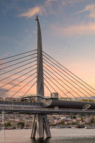 The Golden Horn Metro Bridge in Istanbul, Turkey, features a unique design with a tall, slender tower and a pedestrian walkway. The sunset casts a warm glow over the view photo