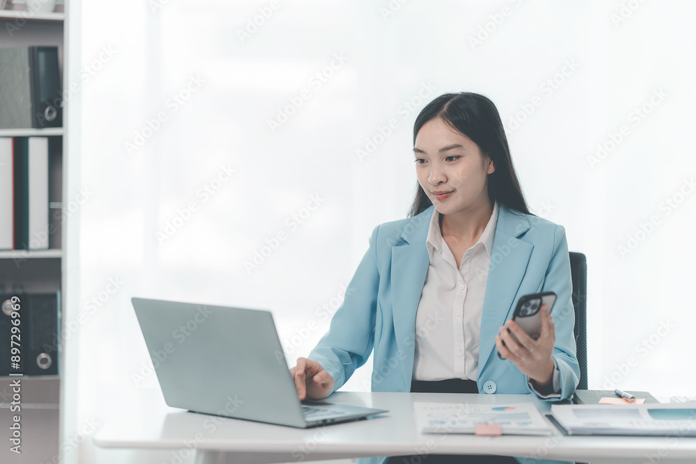 Asian businesswoman using laptop and talking on mobile phone Contact financial businesses online, talk to customers on the phone with a confident demeanor and effective communication skills. Asian businesswoman using laptop and talking on mobile phone Contact financial businesses online, talk to customers on the phone with a confident demeanor and effective communication skills.