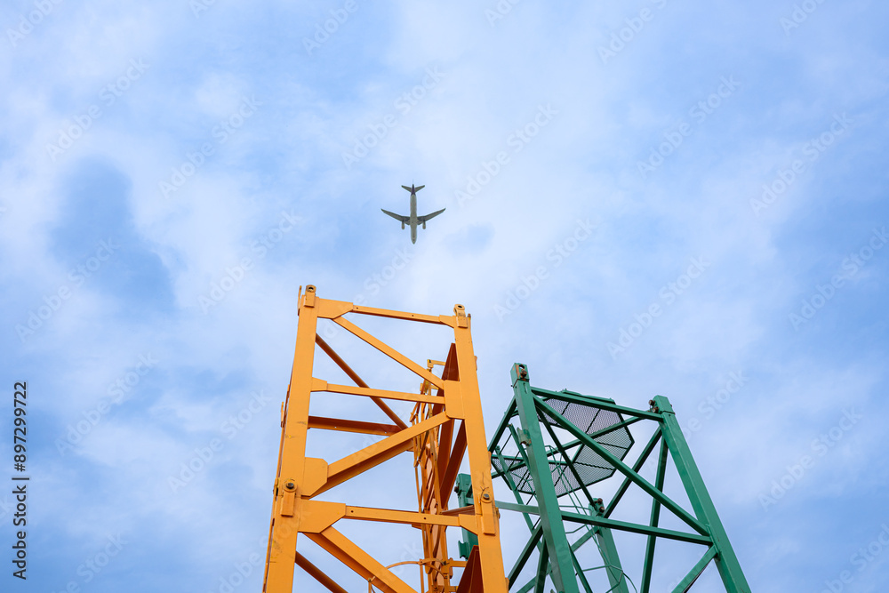 Tower crane in at construction site with air plane on sky in the background Tower crane in at construction site with air plane on sky in the background
