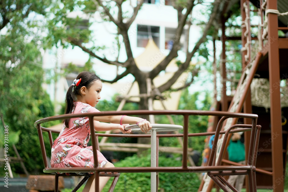 Naklejka premium Adorable little kid in summer time at park having a ride on the merry-go-round.