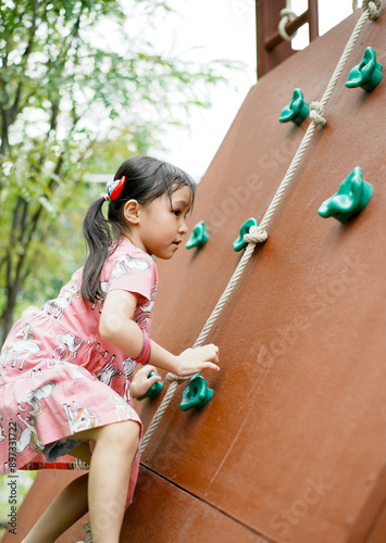 Adorable little girl having fun and climbing on wall at playground. Copy space.