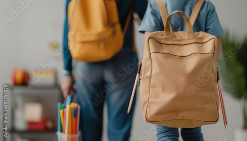 A young student with a brown backpack walks into a classroom. The student is wearing a blue shirt and jeans. The student is carrying a yellow pencil case.
