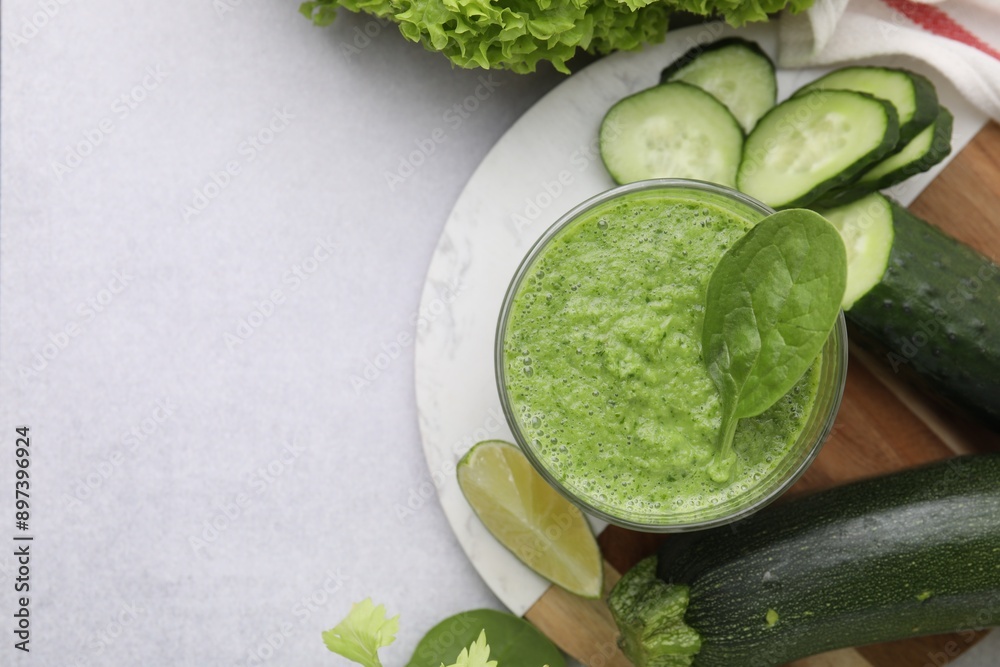 Obraz premium Tasty green smoothie in glass, lime and vegetables on light table, flat lay. Space for text