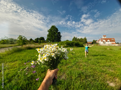 woman running across the field for a bouquet of daisies, field bouquet, happy girl, blue sky, clouds, old houses, woman in sherts, summer photo