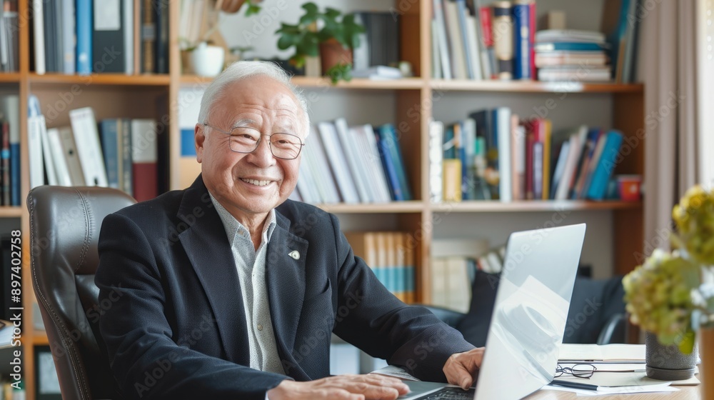 Senior Asian male businessman using laptop at office desk. Concept of elderly professional, technology in workplace, senior employment Senior Asian male businessman using laptop at office desk. Concept of elderly professional, technology in workplace, senior employment