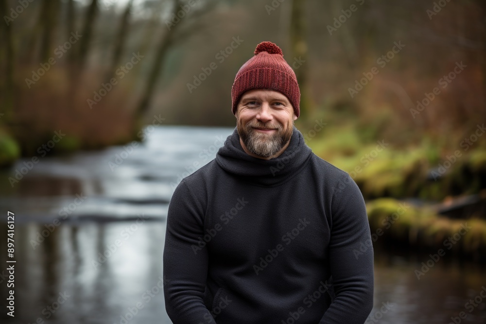 Portrait of a satisfied man in his 40s donning a warm wool beanie isolated on tranquil forest stream Portrait of a satisfied man in his 40s donning a warm wool beanie isolated on tranquil forest stream