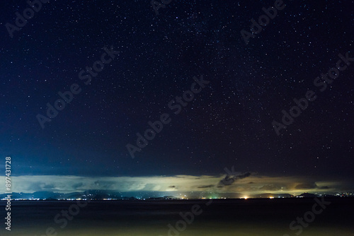 A breathtaking view of a starry night sky over the ocean, with distant city lights illuminating the horizon.