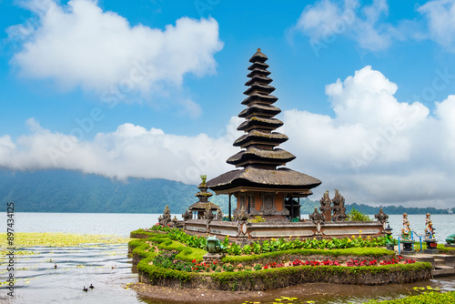 A stunning view of Ulun Danu Beratan Temple in Bali, surrounded by water and lush greenery, under a bright blue sky, showcasing its traditional Balinese architecture. photo