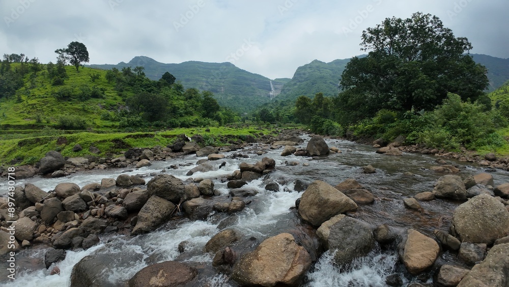 Scenic view of mountain stream cascading over rocks with green hills in the backdrop. Scenic view of mountain stream cascading over rocks with green hills in the backdrop.