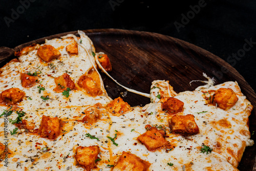 A butter chicken pizza topped with chunks of tender, marinated chicken in a rich, creamy butter sauce. The golden crust is covered with melted cheese and garnished with fresh cilantro, creating a fusi photo