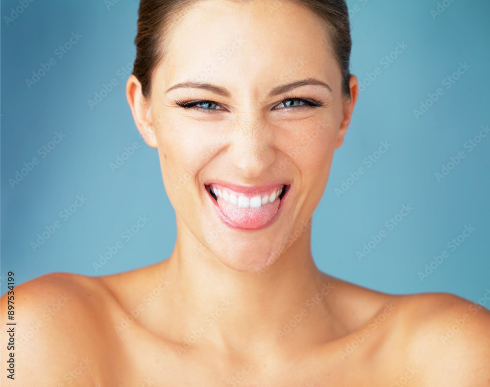 Woman, happy portrait and tongue for beauty with funny expression, natural makeup and skincare in studio. Female person, comedy face and dermatology for shine, smile and skin glow by blue background Woman, happy portrait and tongue for beauty with funny expression, natural makeup and skincare in studio. Female person, comedy face and dermatology for shine, smile and skin glow by blue background