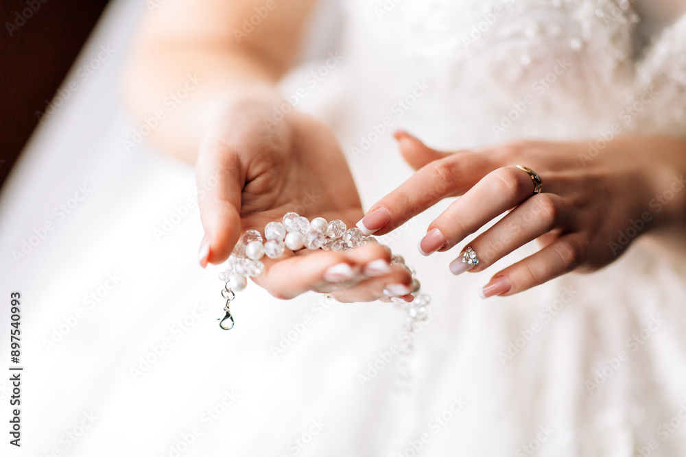 A woman is holding a necklace with a pendant. The necklace is made of pearls and is white in color. The woman is wearing a white dress and has her hands clasped together A woman is holding a necklace with a pendant. The necklace is made of pearls and is white in color. The woman is wearing a white dress and has her hands clasped together