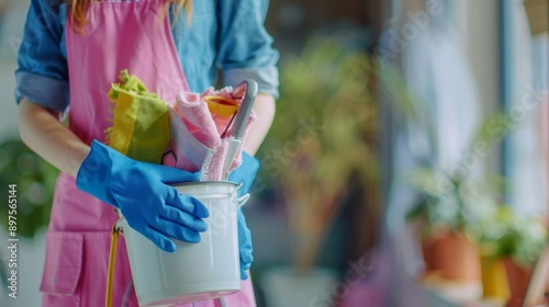 A close-up of a woman holding a bucket of cleaning supplies, including sponges, rags, and a mop. The image represents cleanliness, domesticity, and hard work.