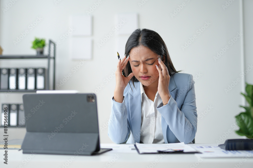 Young asian businesswoman suffering from a headache, touching her temples, feeling tired and overworked in a modern office Young asian businesswoman suffering from a headache, touching her temples, feeling tired and overworked in a modern office