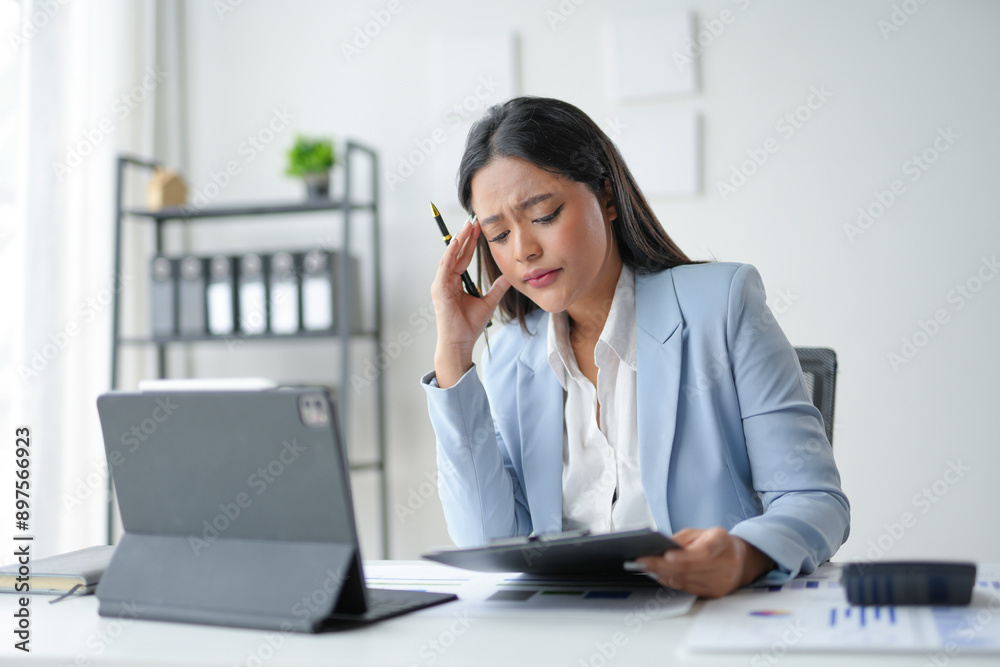Tired businesswoman experiencing a headache, touching her head, feeling stressed and frustrated while working on a laptop in the office Tired businesswoman experiencing a headache, touching her head, feeling stressed and frustrated while working on a laptop in the office