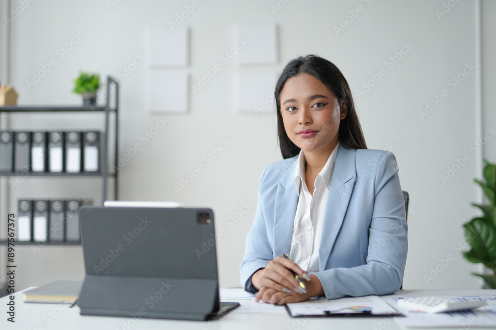 Young asian businesswoman is sitting at her desk in a modern office, holding a pen and working with financial documents Young asian businesswoman is sitting at her desk in a modern office, holding a pen and working with financial documents
