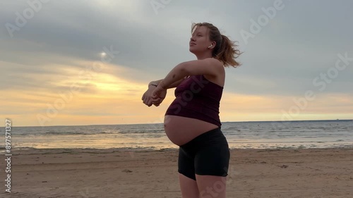 Young pregnant active woman doing exersice outdoors, stratching her body and meditate on the sea, beach at sunset in the evening photo