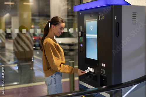 Young woman driver paying for ticket in parking meter near terminal in the underground parking area photo