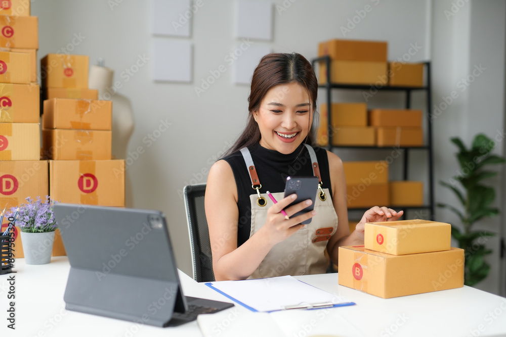 Asian sme business woman is working in her home office, using her smartphone to check a customer order on an online marketplace Asian sme business woman is working in her home office, using her smartphone to check a customer order on an online marketplace