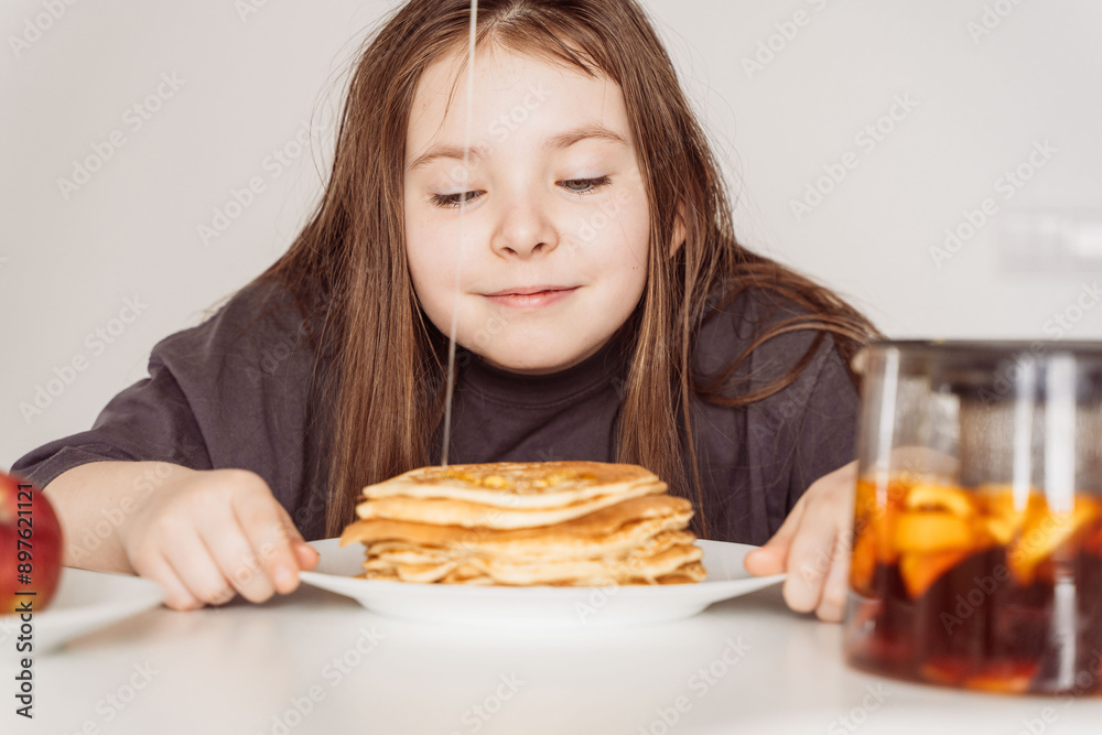 Little girl of pre-adolescence, inhales the aroma of freshly baked pancakes stacked in a stack. Selected focus Little girl of pre-adolescence, inhales the aroma of freshly baked pancakes stacked in a stack. Selected focus