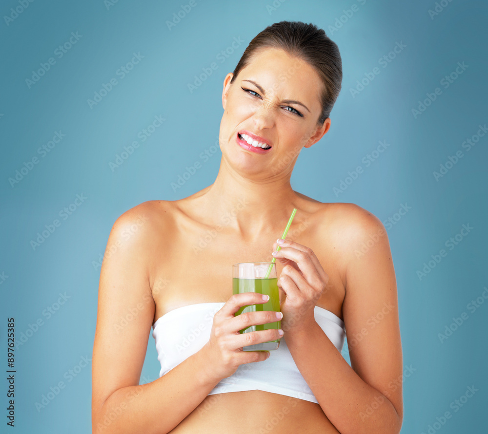 Juice, portrait and woman in studio with disgust for minerals, vitamin C or healthy beverage on blue background. Diet, glass and model with green smoothie for wellness, antioxidants or nutrition Juice, portrait and woman in studio with disgust for minerals, vitamin C or healthy beverage on blue background. Diet, glass and model with green smoothie for wellness, antioxidants or nutrition