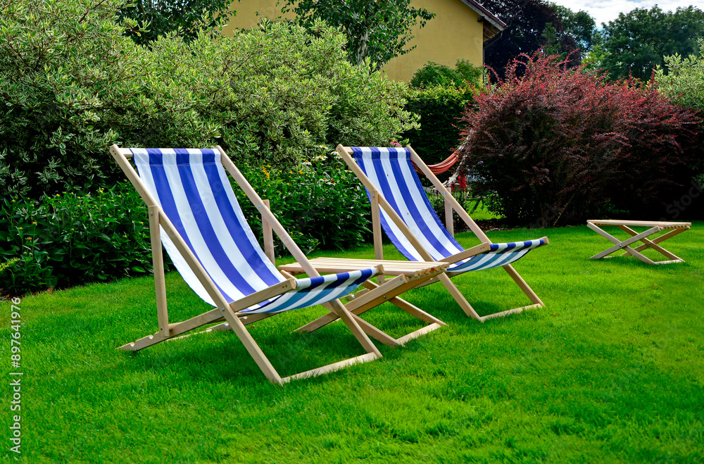leżaki w biało-niebieskie pasy w ogrodzie, leżaki w ogrodzie, kącik wypoczynkowy z leżakiami, blue and white striped deckchairs in garden, deckchairs in the garden, empty deck chairs, seating area