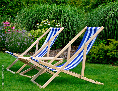 Obraz na płótnie leżaki w biało-niebieskie pasy w ogrodzie, leżaki w ogrodzie, kącik wypoczynkowy z leżakiami, blue and white striped deckchairs in the garden, deckchairs in the garden, empty deck chairs, seating area w salonie