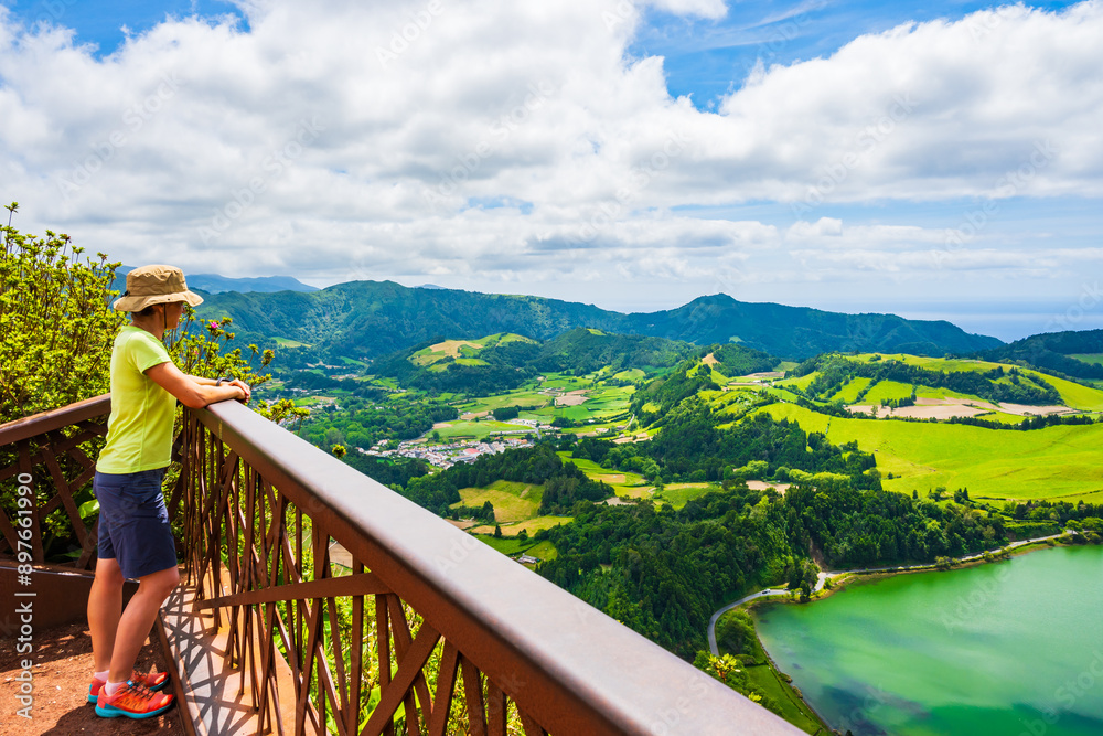 Young woman tourist with sun hat looking at green lake Furnas from Pico do Ferro viewpoint, Sao Miguel island, Azores, Portugal