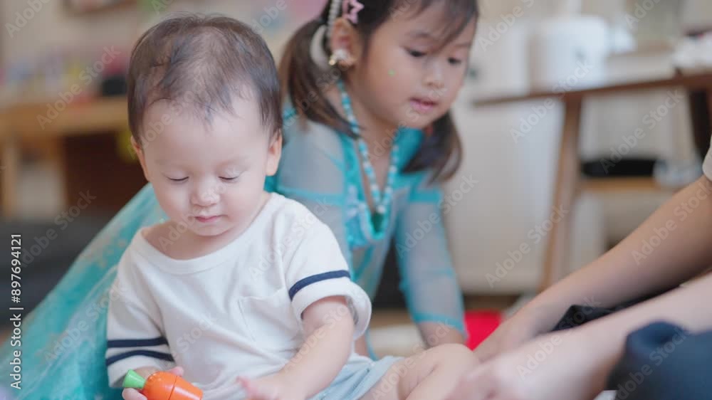 Young asian toddler playing with his sister and mother, family bonding relationship with young new born family members, shot indoors inside cozy house living room, preschool kids kindergarten Young asian toddler playing with his sister and mother, family bonding relationship with young new born family members, shot indoors inside cozy house living room, preschool kids kindergarten