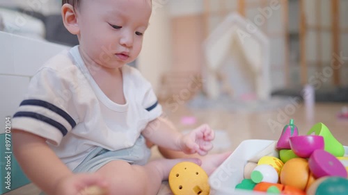 Joyful asian boy sitting inside the living room, asian toddler playing colorful wooden toys alone inside the house, learning development skill, put away in places, collecting organized colorful toys