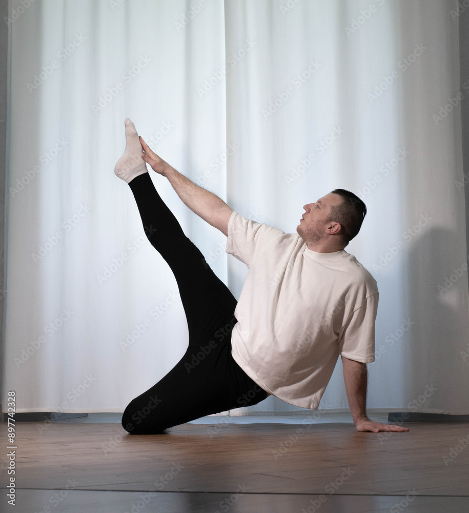 Fototapeta premium Home yoga pose workouts. A man performs sports exercises with his legs and arms. Male athlete stretches.