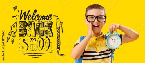 Happy little boy with alarm clock and text WELCOME BACK TO SCHOOL on yellow background