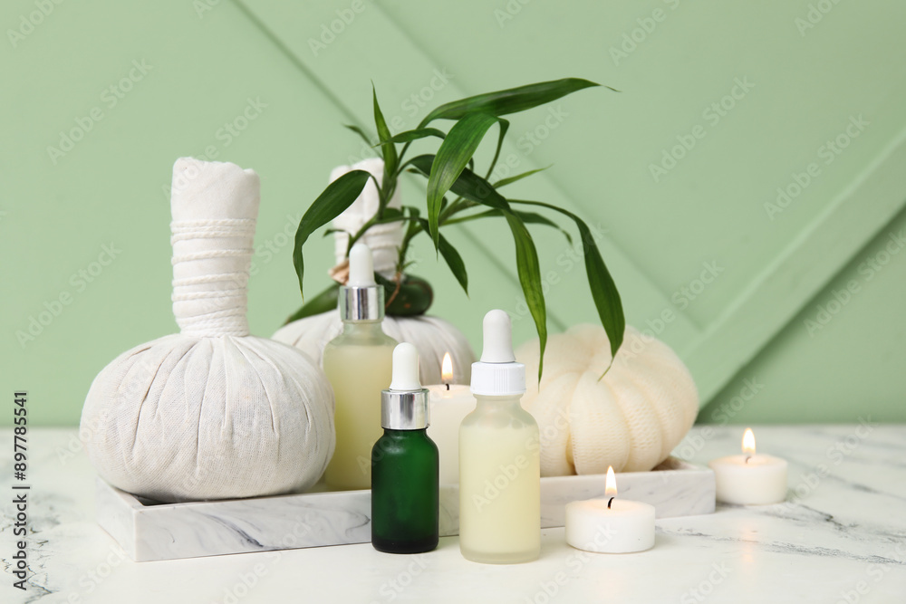 Set of spa supplies with bottles of cosmetic oil, herbal bags, bath sponge and burning candles on white table Set of spa supplies with bottles of cosmetic oil, herbal bags, bath sponge and burning candles on white table