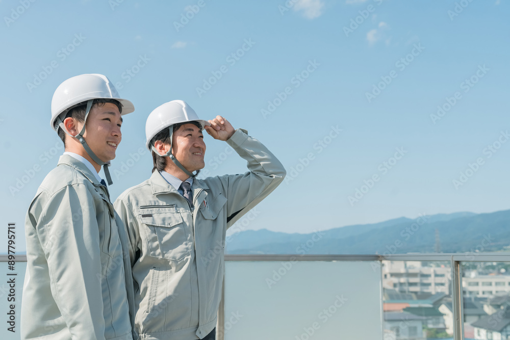 青空の中に立つ作業服を着た作業員（建設・建築・設計・不動産・土木・工事・現場監督・運送）
